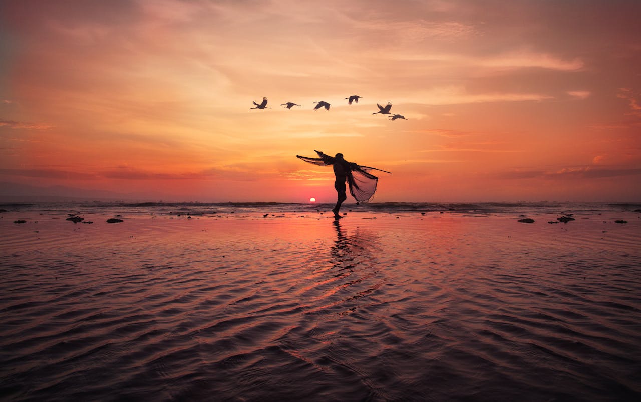Dramatic silhouette of a fisherman with nets at sunset, birds flying over Pimentel beach.