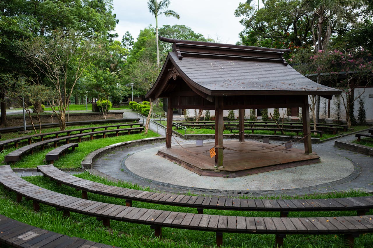 Beautiful wooden Japanese gazebo surrounded by lush greenery in an urban park with seating.