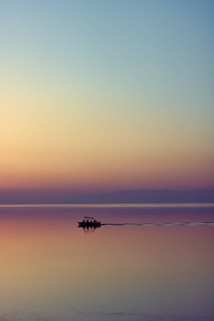 A serene scene of a boat silhouetted against the colorful sunset horizon over calm waters.