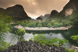 A scenic view of an island with boats, temple, and lush greenery in a tranquil setting.