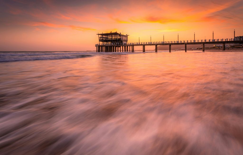 Capture of a beautiful sunset over the ocean with Durban's pier, showcasing vibrant colors and waves.